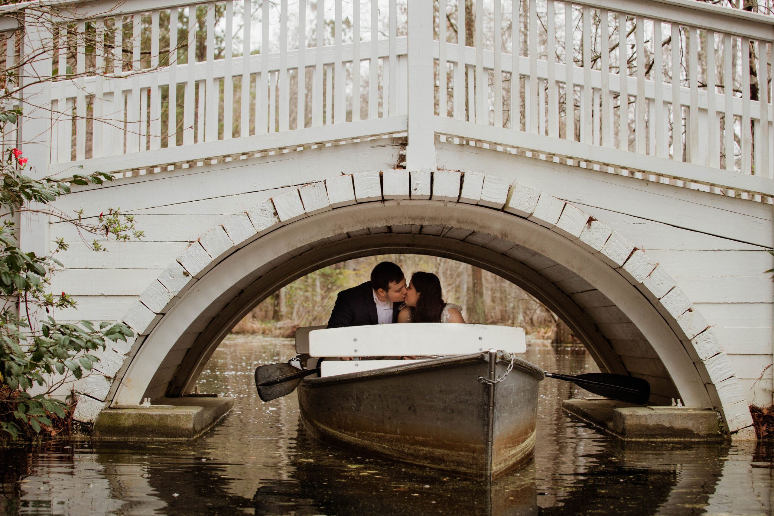 A couple canoes under a white bridge and shares a kiss